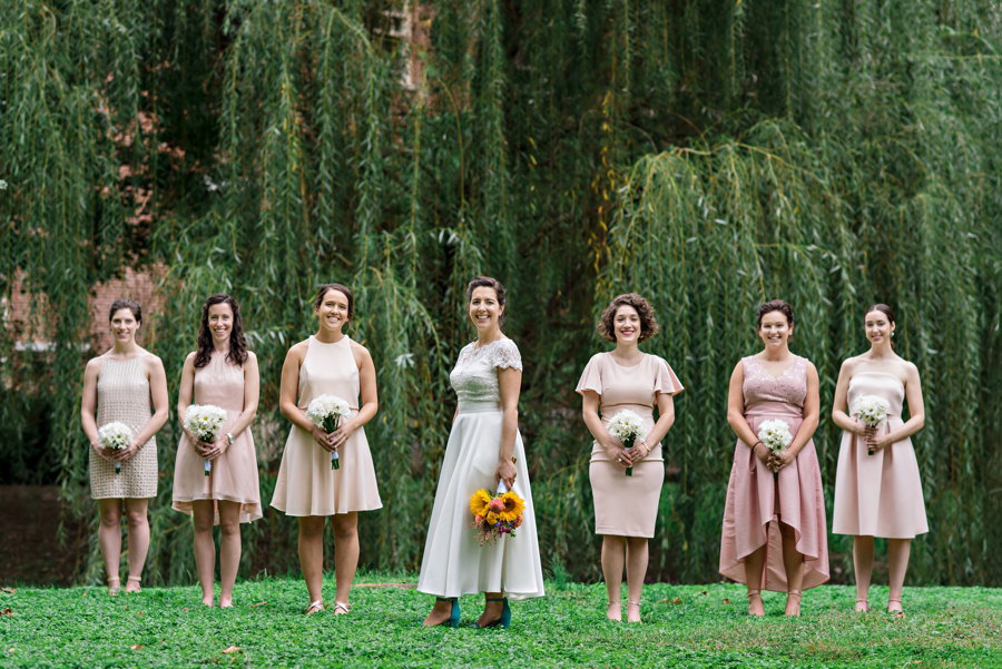 A bride and her bridesmaids pose for a portrait in the grass.